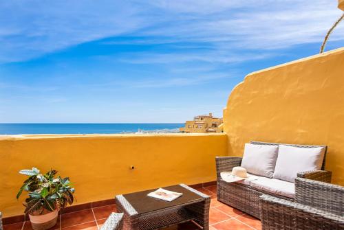 a balcony with a couch and a table and the ocean at Sky And Sea Estepona Penthouse in Estepona