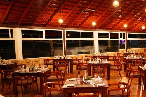 um restaurante com mesas e cadeiras de madeira e janelas em Coorg Orange Blossom Resort and Spa em Suntikoppa