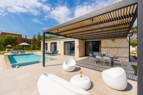 an outdoor patio with white chairs and a pool at Villa Margarita in Katelios