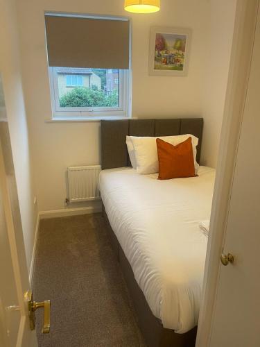 a bedroom with a bed with an orange pillow on it at Homely 3-bed home Milton Keynes in Simpson