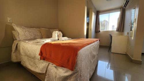 a bedroom with a bed with an orange blanket on it at Hotel Areião in Goiânia