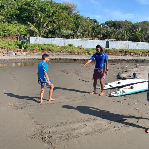 two men standing on the beach with a surfboard at Surf Lodge El Carrizal-Punta Mango in La Periquera