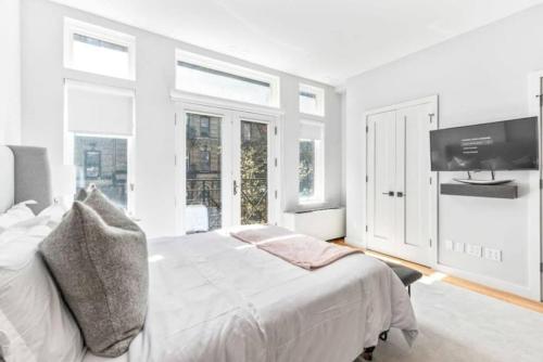 a white bedroom with a bed and a flat screen tv at Luxe Studio w Juliet Balcony in Upper East in New York