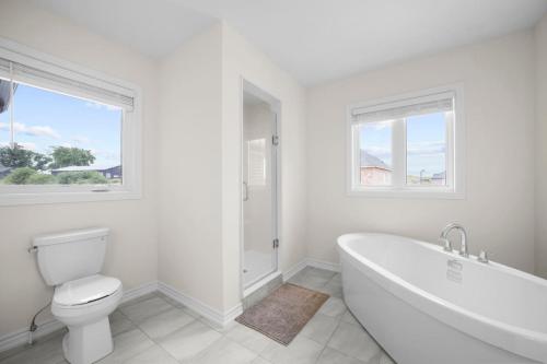 a white bathroom with a tub and a toilet at Prime Peterborough - 4BR and Office, Newly Renovated in Peterborough