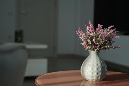 a white vase with pink flowers sitting on a table at Mirandis Apartments - Modern Stays with Free Parking near Coresi Mall in Braşov