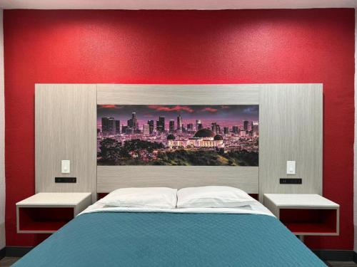 a bed with a red wall with a picture of a city at Playa Inn Motel - Long Beach, LA in Long Beach