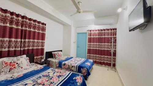 a bedroom with two beds and a tv and curtains at Mohammadia Restaurant & Guest House in Dhaka
