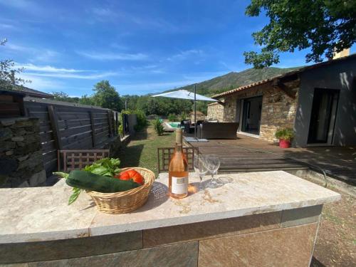a table with a bottle of wine and a basket of vegetables at Villabergerie En Pierre Du Pays in Barbaggio