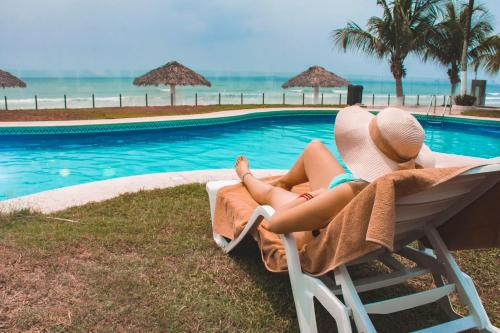 a woman sitting in a chair next to a swimming pool at Playa Caracol Hotel & Spa in Veracruz