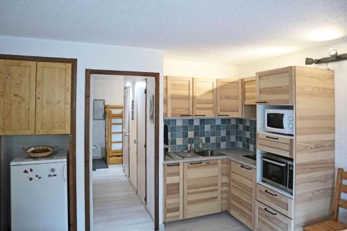 une cuisine avec des armoires en bois et un réfrigérateur blanc dans l'établissement Résidence Le Pouzenc - Studio 6 personnes 1650 MAE-9581, aux Orres