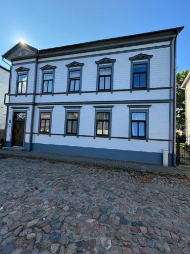 a white building with windows on a cobblestone street at 550 метров до моря in Liepāja