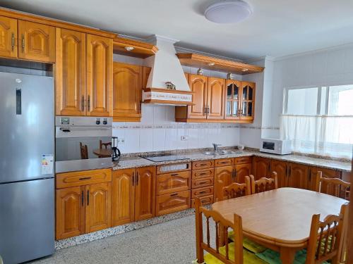 a kitchen with wooden cabinets and a table and a refrigerator at Piso Beiramar O Grove in O Grove