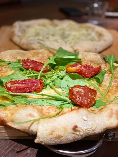 two pizzas with pepperoni and greens on a table at Hospedagem Tulipane - Praia do Campeche in Florianópolis
