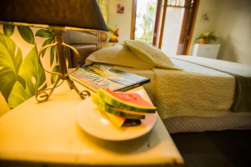 a sandwich on a plate on a table next to a bed at Hospedagem Tulipane - Praia do Campeche in Florianópolis