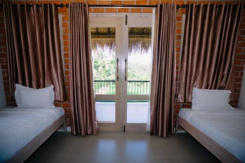 a room with two beds and a door with a window at Novia Guest House Lombok-Tetebatu in Tetebatu