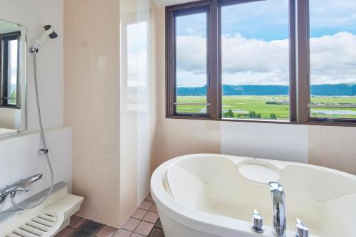 a white bathroom with a tub and a window at Kamenoi Hotel Aso Park Resort in Aso