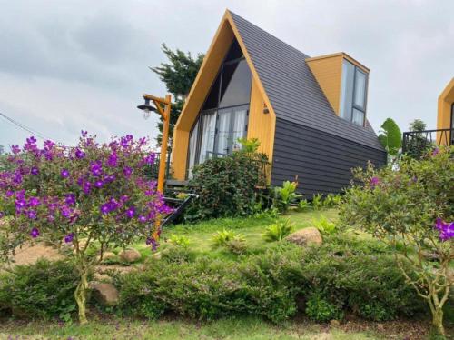 a house with a black roof and purple flowers at Làng OMM Homestay - Venuestay in Tang Klang