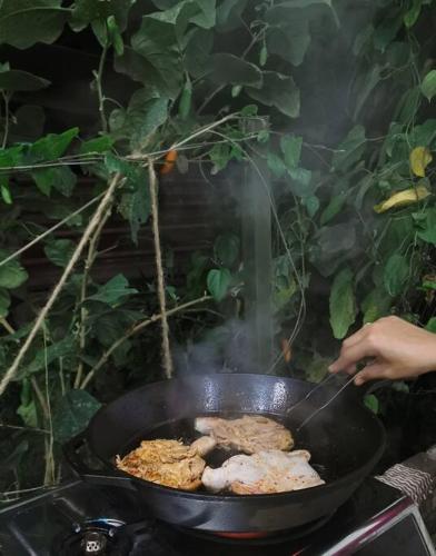 a person cooking food in a pan on a grill at Tirtha Quddus Farm Stay in Kampong Sum Sum