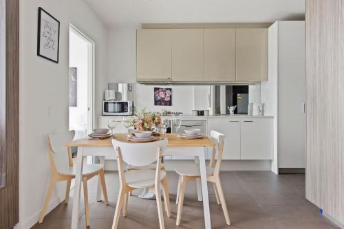 a white kitchen with a wooden table and chairs at A Cozy 2BR Apt with Harbour Views FREE Parking in Melbourne