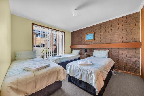 two beds in a room with a brick wall at Anchorbell Apartments Merimbula in Merimbula