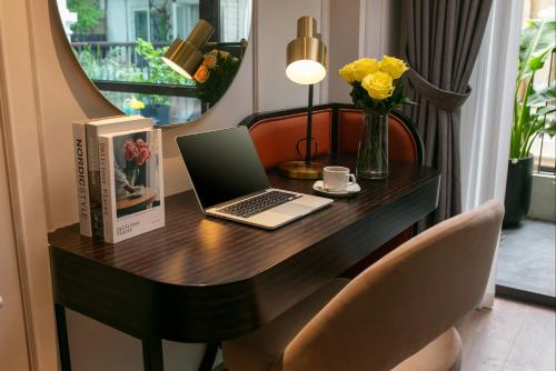 a desk with a laptop and a vase of flowers at Le Premier Hotel & Rooftop Bar in Hanoi
