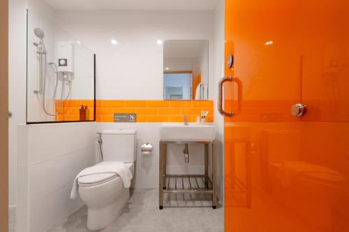 an orange and white bathroom with a toilet and a sink at Moji Don Mueang Airport Hotel - Bangkok in Bangkok