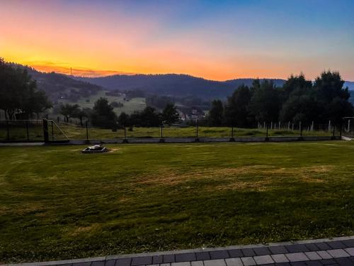 a sunset over a grassy field with the mountains in the background at Beskidzki Domek Kurów in Kurów