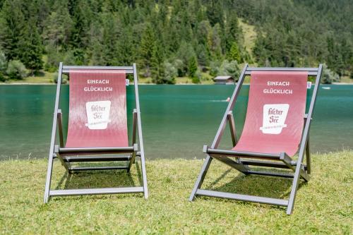 two chairs sitting on the grass next to a lake at Hotel Fischer am See in Heiterwang