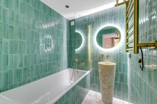 La salle de bains est pourvue de murs carrelés verts, d'une baignoire et d'un miroir. dans l'établissement Splendide appartement à Avenue Achille Peretti II, à Neuilly-sur-Seine