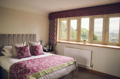 a bedroom with a bed with a pink comforter and windows at The Manor Boutique Hotel Restaurant and Bar in Conwy