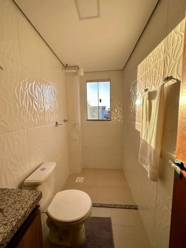 a white bathroom with a toilet and a window at Zaffir Apartamento in Cuiabá