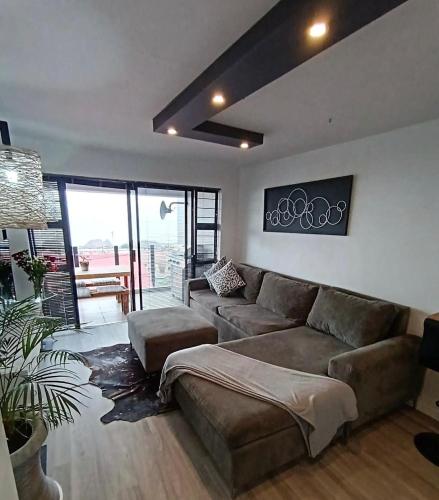 a living room with a sectional couch and a table at Modern 1 Bedroom Apt & Sauna Flowerbox Triton Heights in Mossel Bay