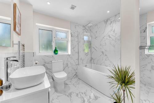 La salle de bains blanche est pourvue de toilettes, d'une baignoire et d'un lavabo. dans l'établissement Garden Cottage, à Cuddington