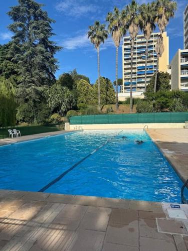 une grande piscine bleue avec des palmiers et des bâtiments dans l'établissement Terrasses de la Corniche, 2p 65m2 spacieux, terrasses mer & montagne, piscine et parking privé, à Nice