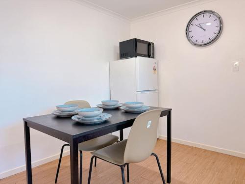 a dining room table with chairs and a clock on the wall at Comfy unit near Garden City Westfield Street Parking in Brisbane
