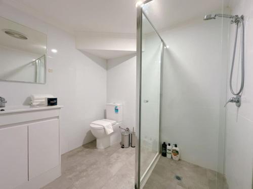 a white bathroom with a shower and a toilet at Comfy unit near Garden City Westfield Street Parking in Brisbane