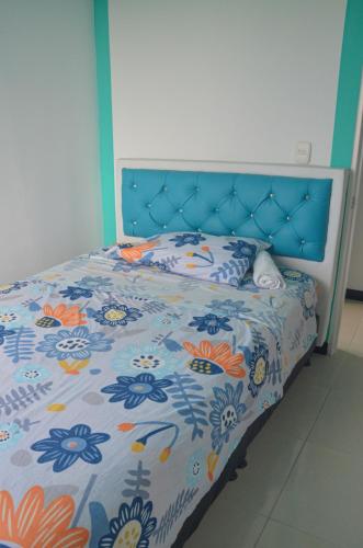 a bed with a blue head board with a floral bedspread at SANDY APARTAMENTO in Santa Rosa de Cabal