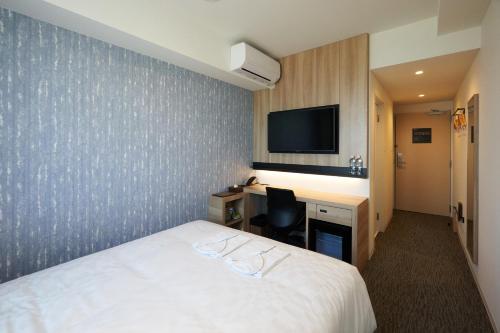 a hotel room with a bed and a desk and a tv at Henn na Hotel Komatsu Ekimae in Komatsu