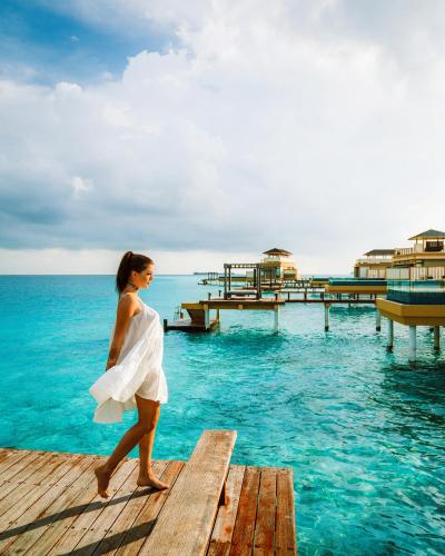 a woman walking on a dock in the water at Angsana Velavaru in Dhaalu Atoll