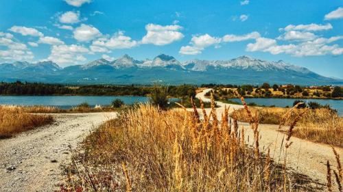 a dirt road next to a body of water with mountains at StoneMlynska 7 Slovakia in Svit