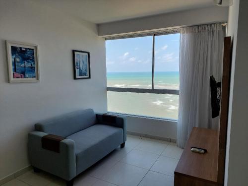 a living room with a blue couch and a large window at Marinas da Barra - Flat Beira-Mar em Barra de Jangada por Yolo in Recife
