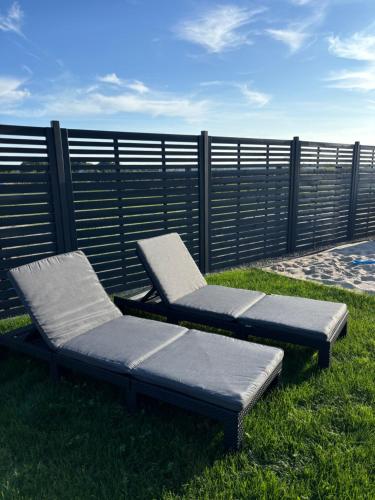 two lounge chairs sitting in the grass next to a fence at Wodne Widoki - domek letniskowy z jacuzzi in Dziwnówek