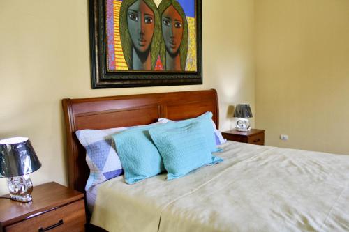 a bedroom with a bed with blue pillows and a painting at Villa-Agapito GuavaberryJuanDolio-11Px-3BR-5Bds-WiFi-BBQ-PrivatePool in Los Conucos