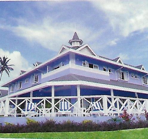 a large white building with a palm tree in front of it at Villa Ananda Tobago in Patience Hill