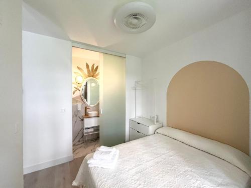 a white bedroom with a bed and a mirror at El Jardín de María Luisa Suites in Burgos