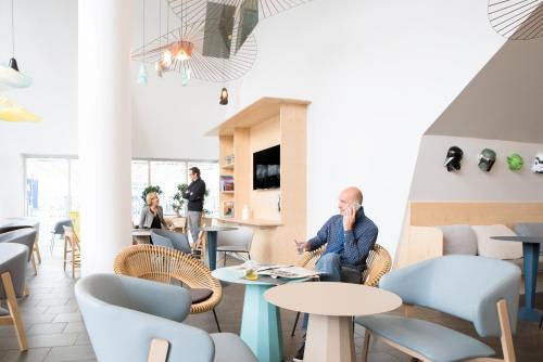 a man sitting in a room with tables and chairs at Novotel Suites Lille Europe in Lille
