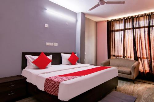 a bedroom with a bed with red pillows and a chair at Hotel O Manya Stay in New Delhi
