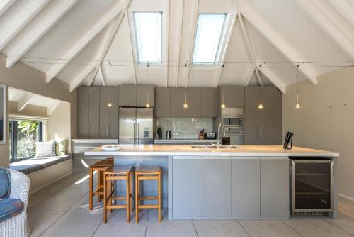 a kitchen with white cabinets and a island with bar stools at Onetangi Beach Pavilion -100 metres to Onetangi Beach! - Be My Guest Waiheke in Onetangi