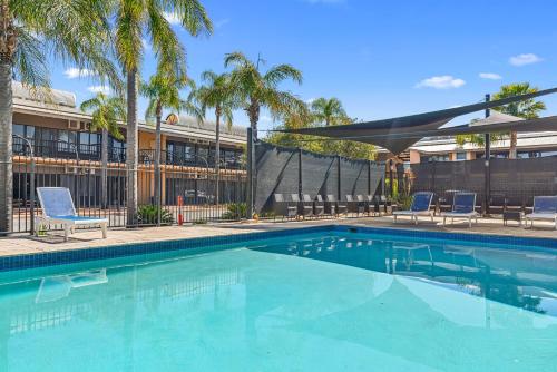 a swimming pool with chairs and palm trees next to a building at Diplomat Hotel Alice Springs in Alice Springs