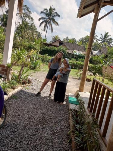 two women and a baby standing next to a house at Stay Together in Tetebatu